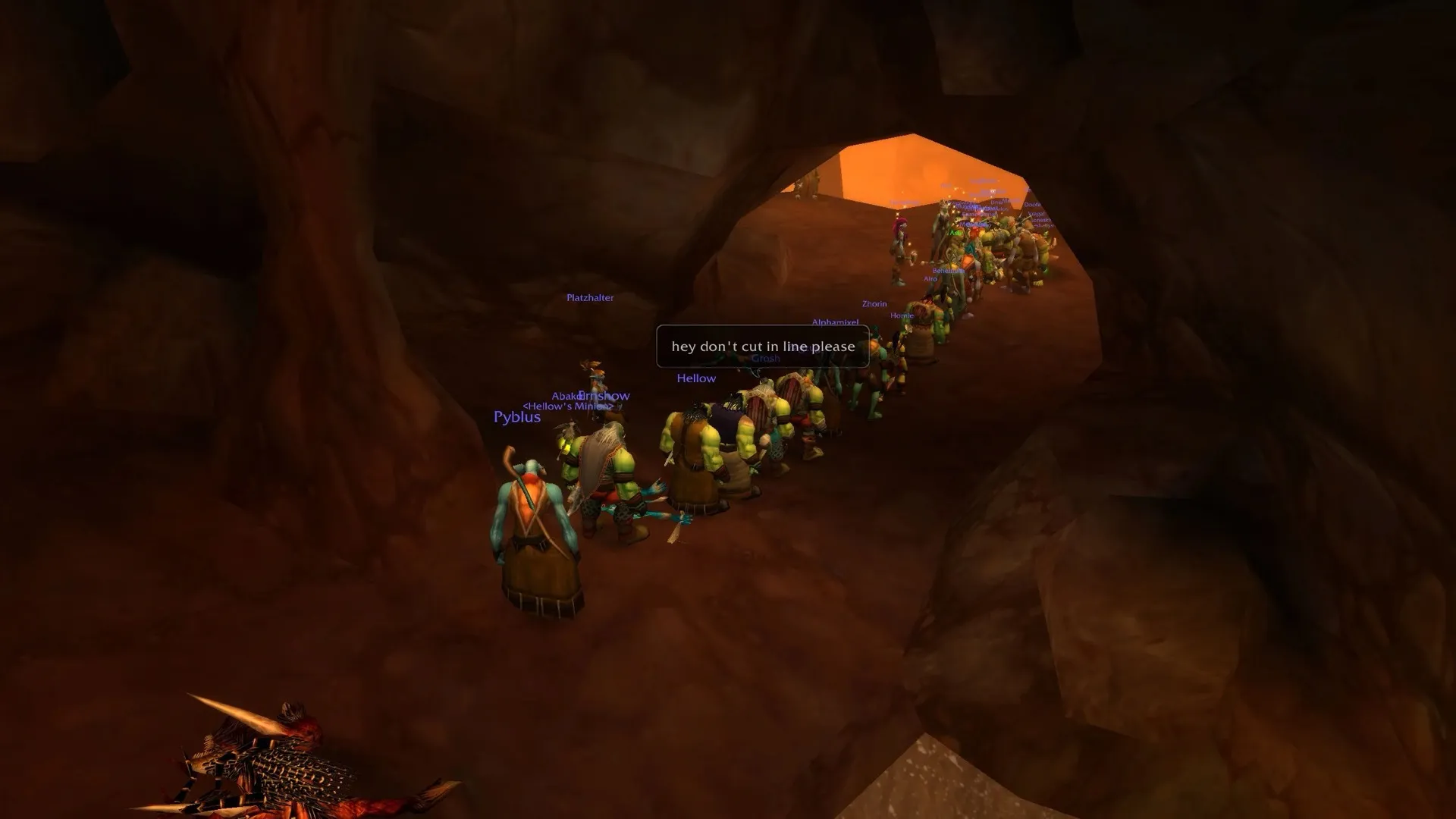 Une longue file de joueurs attend un monstre de quête dans un tunnel de grotte, avec la bulle hey don't cut in line please, une capture d'écran de World of Warcraft
